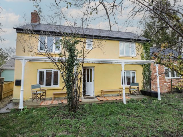 An exterior view of a yellow house with a lawn and seating area at Ambercote in Priors Marston near Southam
