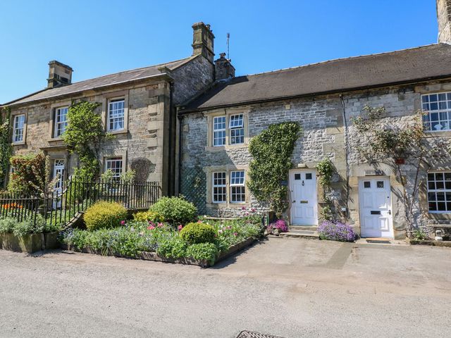 A stone building with flower beds and doors at Ivy Cottage in Hartington