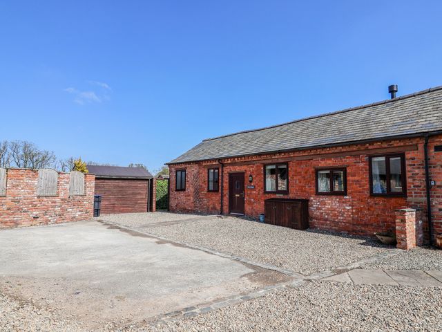 An outdoor view of a brick house with a garage and gravel driveway at Elwy Cottage St Asaph