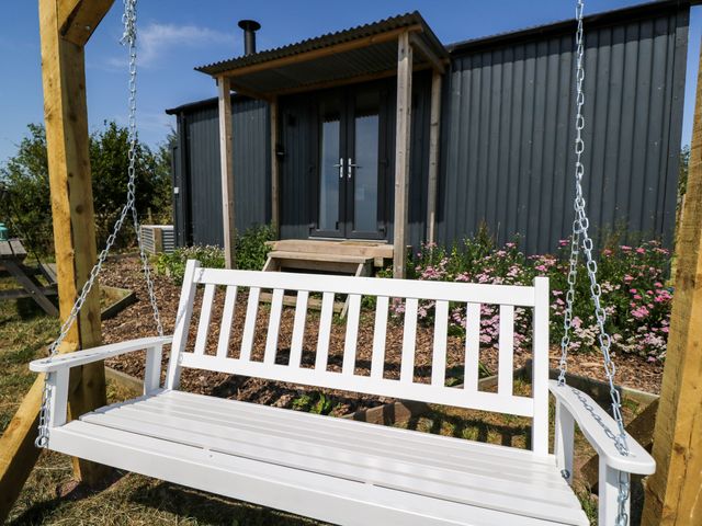 A swing bench with a building in the background at Hares Hideaway Shepherd's Hut South Molton