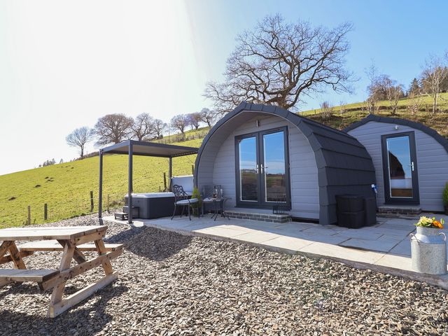 An outdoor area with two log cabins and a hot tub at Cennin Pedr in Ruthin