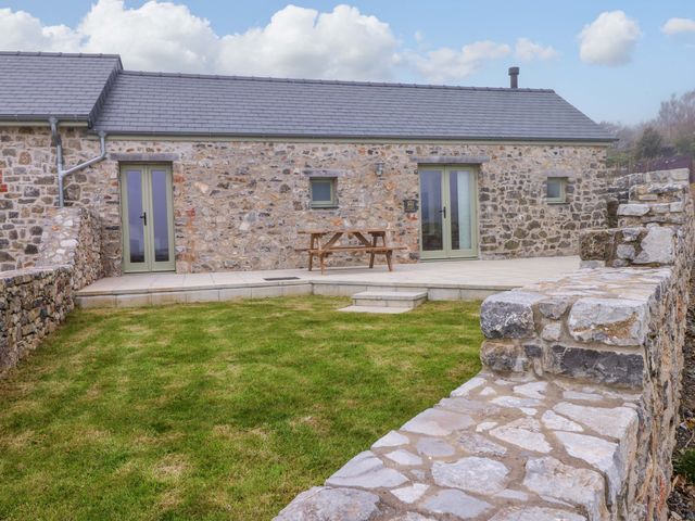 An outdoor area with a stone house and a table at Dairy Cottage in Oxwich