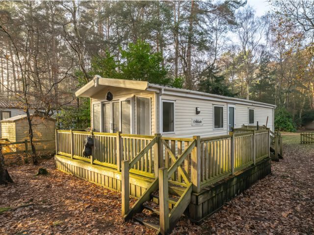 A mobile home with a deck surrounded by trees at Rawsons Retreat - Kelling Heath Holiday Park in Holt
