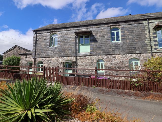 An outdoor view of a stone building with green windows and a fence at Linhay Barn Callington