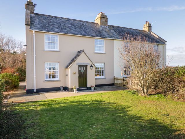 A house with a front door and windows surrounded by grass and bushes at 2 Old Coastguard House Beaumaris