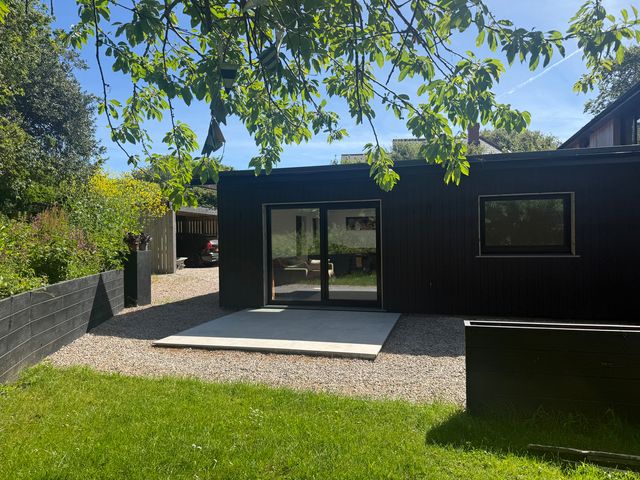 A garden with a black building featuring doors and patio at Birdsong Gulval