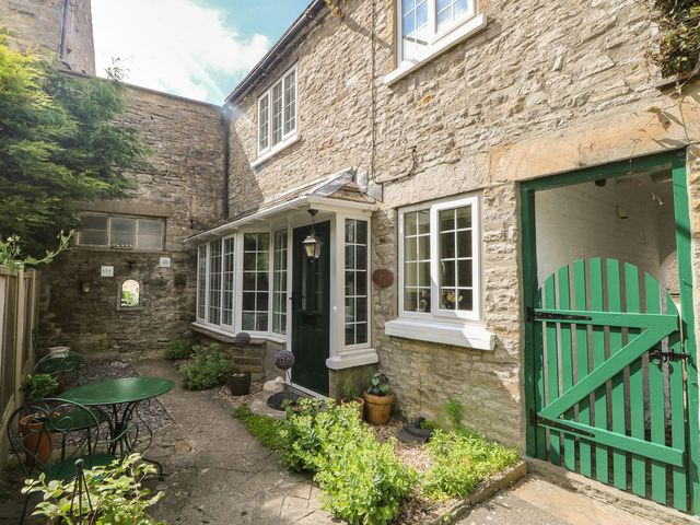 A garden with stone walls and a green door at Wedgewood Cottage in Middleham