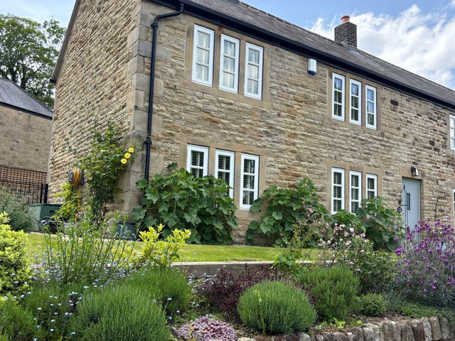 A stone house with flowers and plants in the garden at Holly Cottage in Totley