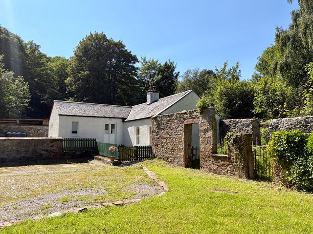 A cottage with a stone wall and garden at Laundry Cottage in Strathpeffer