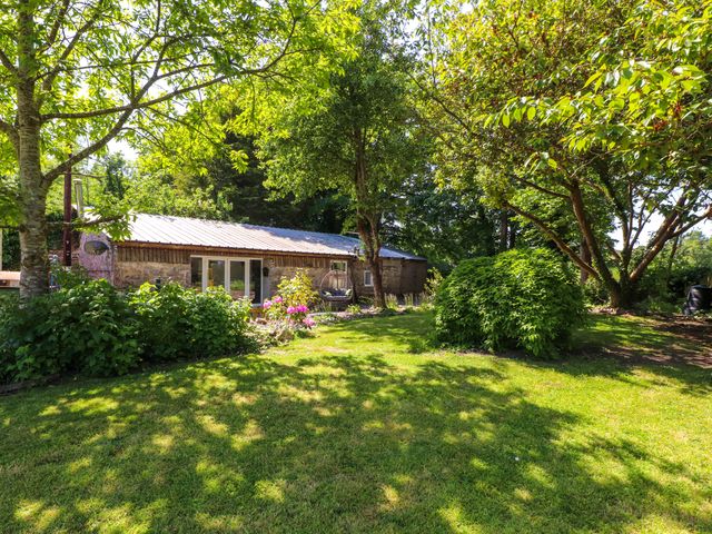 A garden with a building and greenery at Woodman's Lodge in Llanallgo near Moelfre