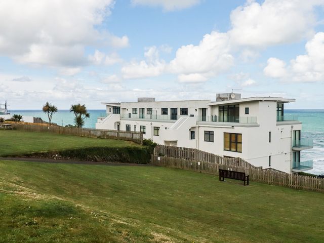 A building near the ocean with grass and a bench at A5 Bay Apt.