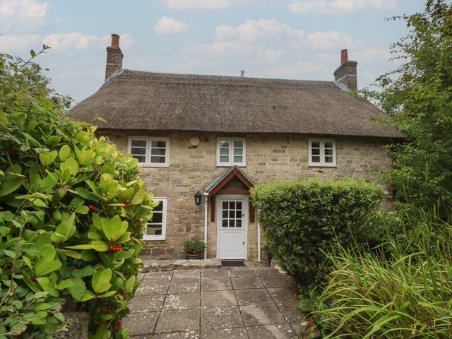 A house with a thatched roof and stone walls at Woodbine Cottage in Weymouth