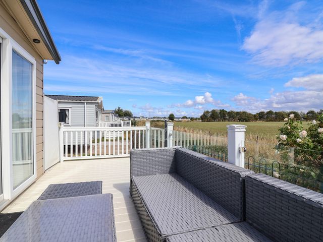 A deck with a sofa and table overlooking a field at Caravan i35 Towyn