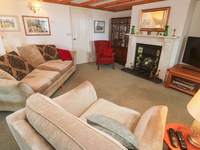 A living room with a sofa, armchair, and fireplace at Chyrose Farmhouse in Pendeen