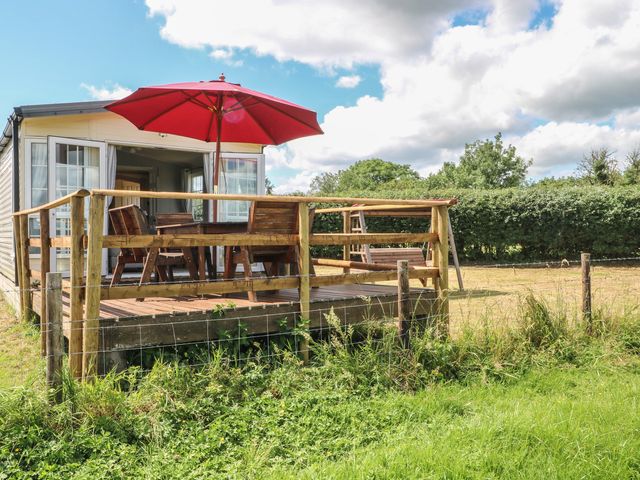 A caravan with a wooden deck and table under an umbrella at Hawks View Caravan in Leek