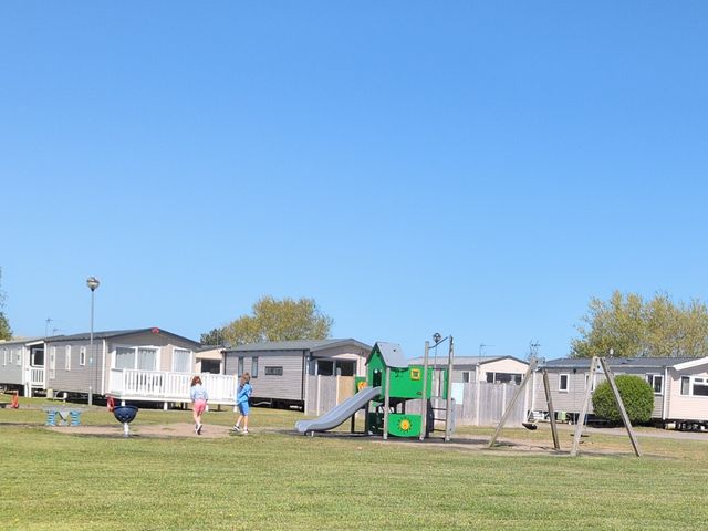 A playground with a slide and swings near caravans at Presthaven - Denbigh Dunes, Prestatyn