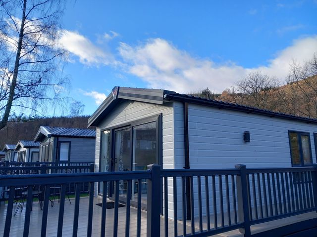 A cabin with a deck and railing at Rowan in Crieff