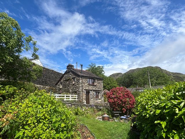 A stone cottage surrounded by flowers and mountains at Over Brow Cottage in Coniston