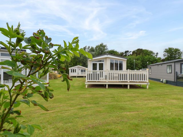 A cabin with a deck surrounded by grass and trees at Finch 66 Scarborough