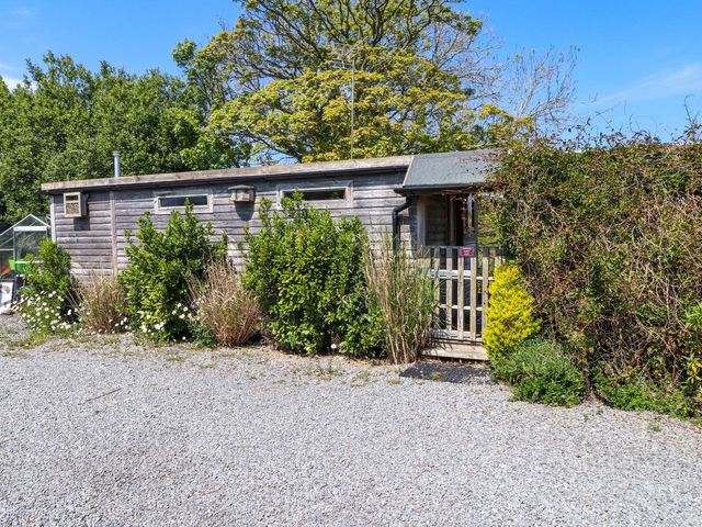 A wooden cabin with a fence and bushes at The Cabin in Amlwch