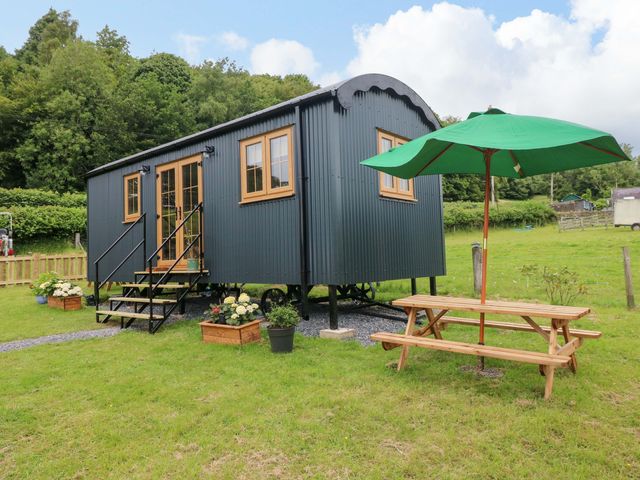 A shepherd hut with steps and a green umbrella in the garden at Shepherd Hut 2
