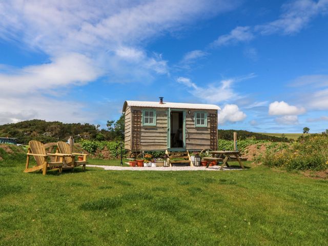 An outdoor cabin with a door and chairs at Cwt Bugail Pwllheli
