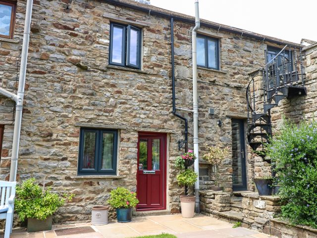 An outdoor view of a stone wall with a red door and windows at Kernot Cottage Reeth