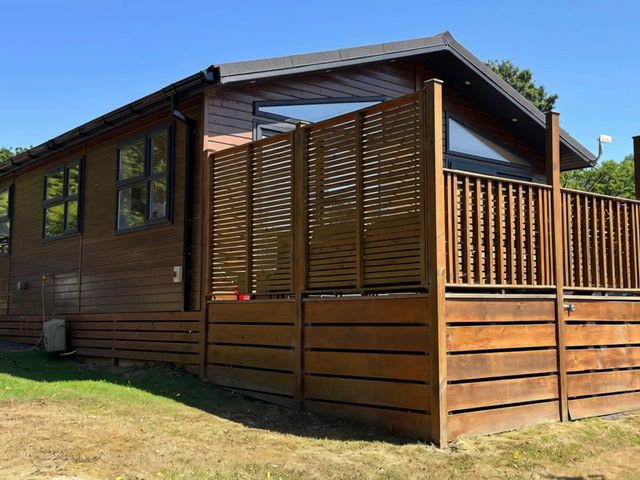 A wooden house with a deck and fence at Lakeside Retreat in Newton Abbot