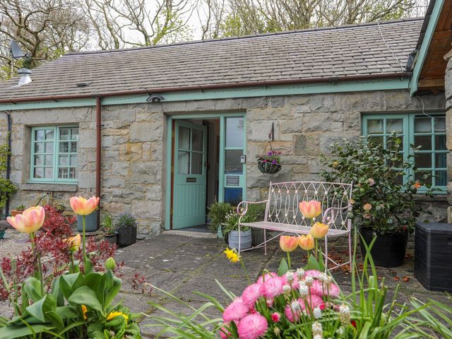 A stone cottage entrance with flowers and a bench at Riverside Cottage in Caernarfon
