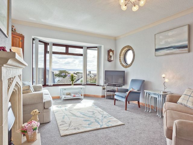 A living room with a sofa and armchair by a bay window at Lothlorien in Grange over Sands