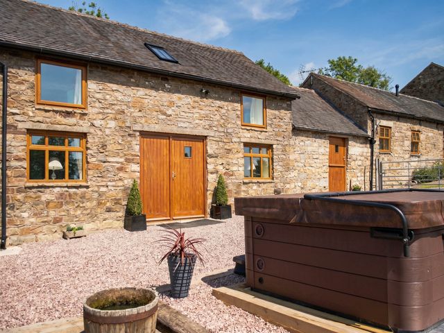 An outdoor area with a stone building and a hot tub in front at a rural property