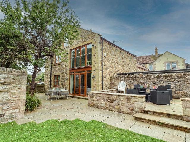 An outdoor patio with stone wall and furniture at Alma House in Seahouses