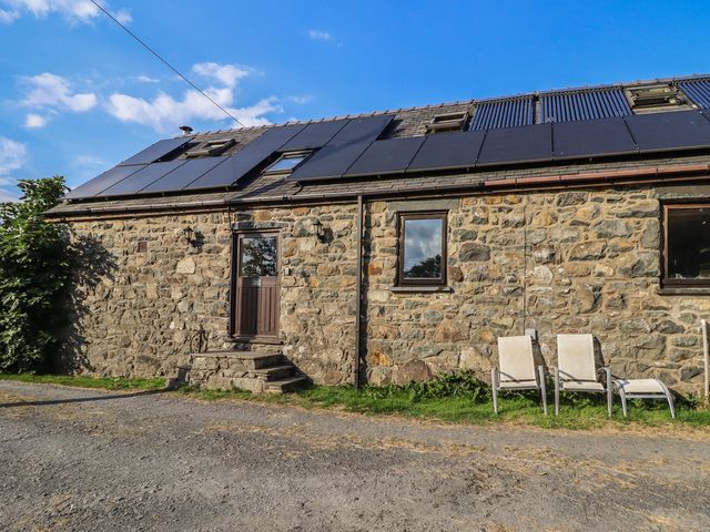 An outdoor view of a stone building with solar panels and chairs at Pandy Farmhouse