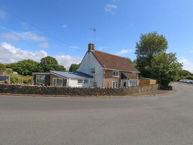 A house with a fence and trees beside the road at Greenwich Cottage in Burton Bradstock