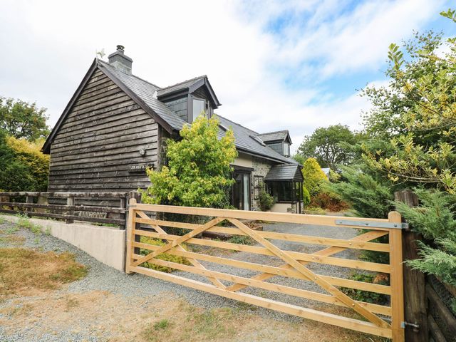 A house with a wooden gate and surrounding trees at Penrhiwoli Barn Cefn Gorwydd
