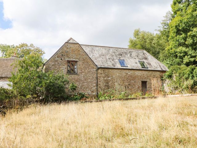 A stone house with a pitched roof and windows surrounded by grass at The Hayloft at Manaton