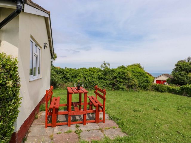 A table and benches with grass and bushes at Cottage 28 in Brixham