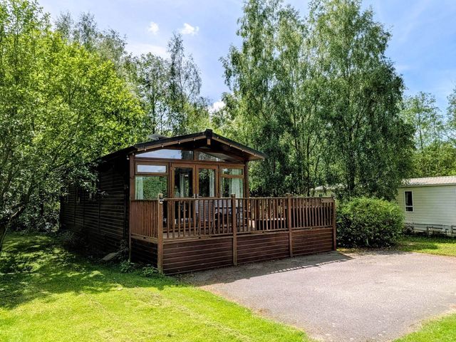 A cabin with a deck surrounded by trees at Felmoor Park Northumberland Lodge with Hot Tub Felmoor Park near Felton