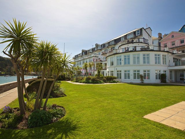 A garden with palm trees and a building by the water at 4 The Salcombe in Salcombe