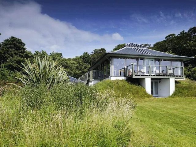 A house with a balcony surrounded by grass and trees at Tigh na Mara Sleeps 4 Sea Views Pet Friendly Drimnin near Lochaline