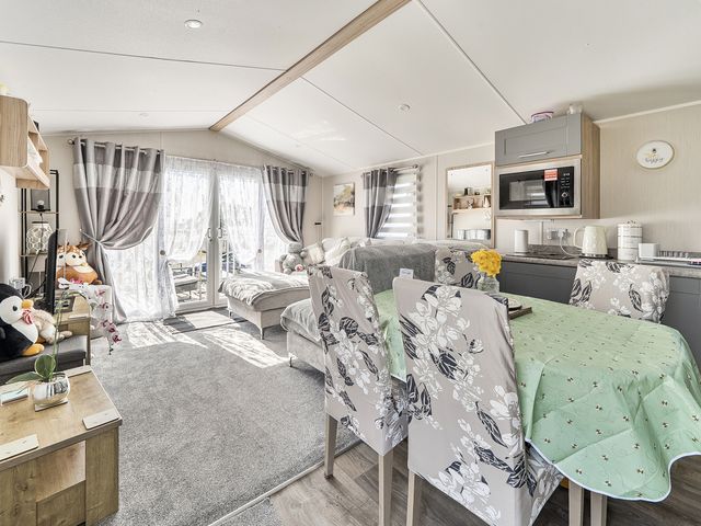 A living room with a sofa dining table and microwave at Cayton Bay Holiday Park Kestrel40, Cayton Bay