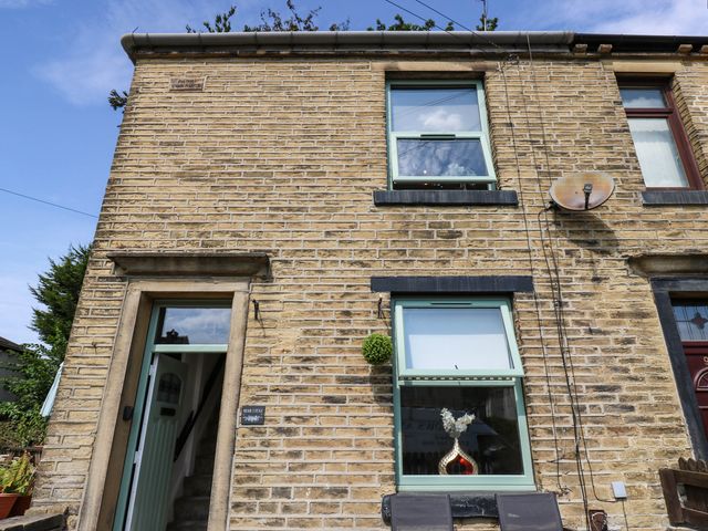 An exterior view of a stone house with windows and a door at Brodie Cottage in Brighouse