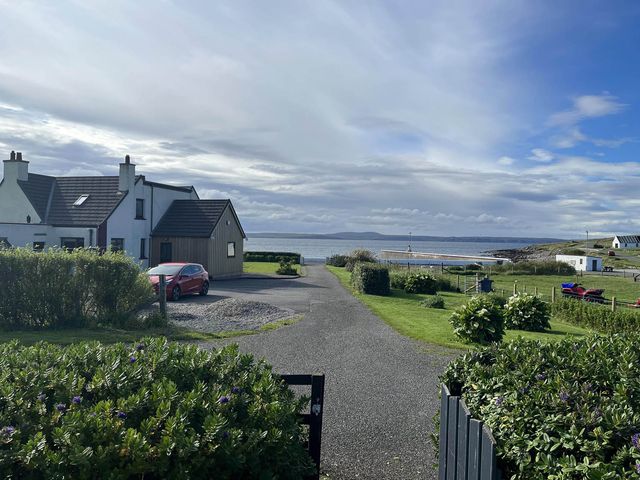An outdoor area with a house and a car near the ocean at a coastal location