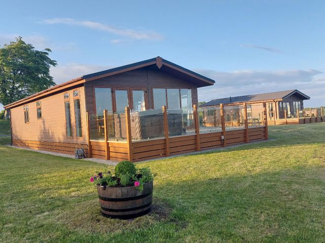 An outdoor view of lodges with decking and garden at 2 Bedroom Sleeps 4 Lodge Smart Tv Hot tub Dogs Ok near Lochwinnoch