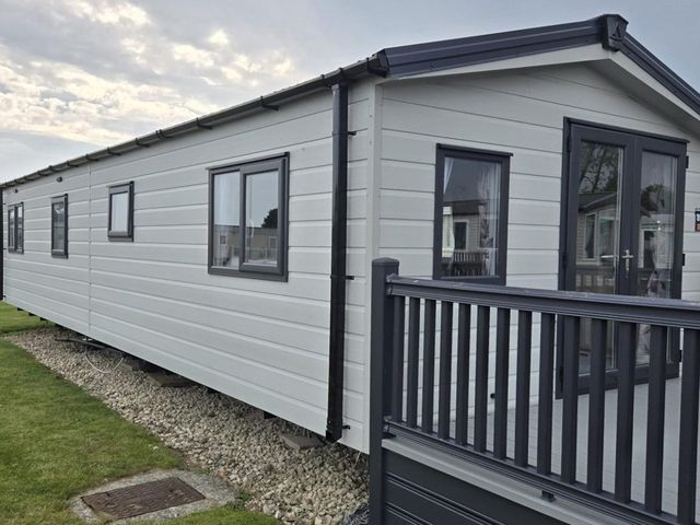 A mobile home with a deck and windows at 3 Bedroom Cabin Sleeps 6 - Shared Pool & Shared Hot Tub, Flamingo Land Resort near Malton