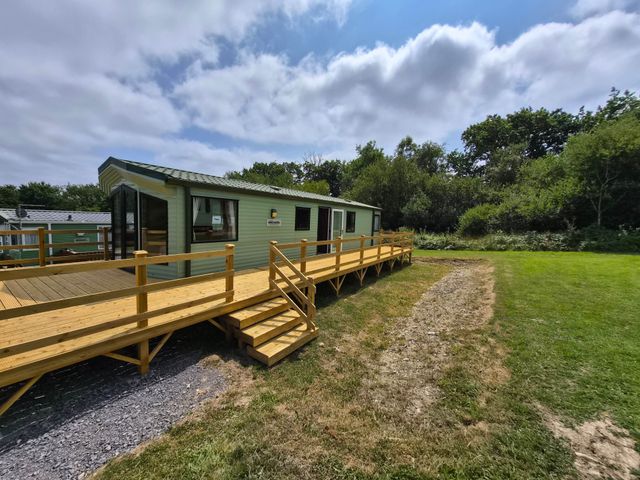 A cabin with a deck and steps in a grassy area at Cabin - Sleeps 6 - Outdoor Pool and Parking Cenarth