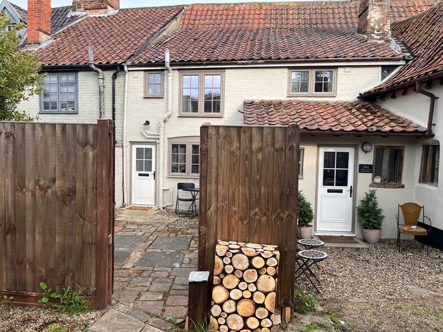 A garden area with a door, seating, and logs stacked at Historic Cottage on the Suffolk border, Harleston Norfolk