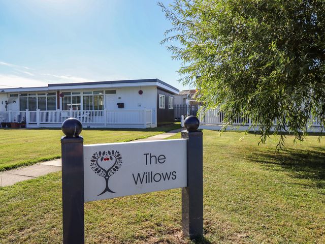 A sign for The Willows in front of a building with grass and trees