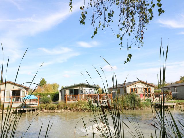 Cabins by a lake with decking and reeds at Patos y Nosotros in Grantham