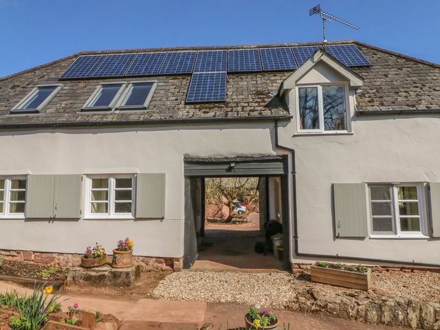 An exterior view of a house with solar panels and a gravel pathway at Upper Barn Cottage in Minehead